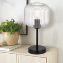 BOBO Black /Cear Table lamp with a glass shade on a wooden surface next to a plant and books.