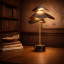Mapel LED Table Lamp with antique brass finish, black marble base, integrated warm white LED lighting and touch dimmer control A Decorative table lamp with a unique design on a wooden surface, with books in the background.