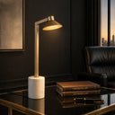 SATROM Antique Brass/white Marble   desk lamp on a dark surface with books and a pen, in a room with a cityscape view.