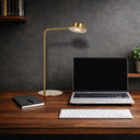 Tarell LED Table Lamp in Antique Gold with gesture-controlled dimming and warm 3000K LED lighting on a Modern desk setup with laptop, keyboard, notebook, and gold lamp on a wooden surface.