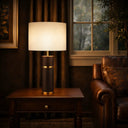 VALDA Table Lamp on a wooden table in a dimly lit room with a leather sofa and window in the background.