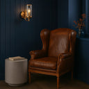Velden Wall Light in rich copper finish with glass shade  in a room with dark blue walls, a small table, and a wall sconce and brown leather chair.