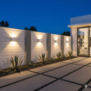 Martec Torino Tricolour LED Wall Light in a Modern outdoor setting with a white fence, plants, and a building at night from Lights and Fans Online 
